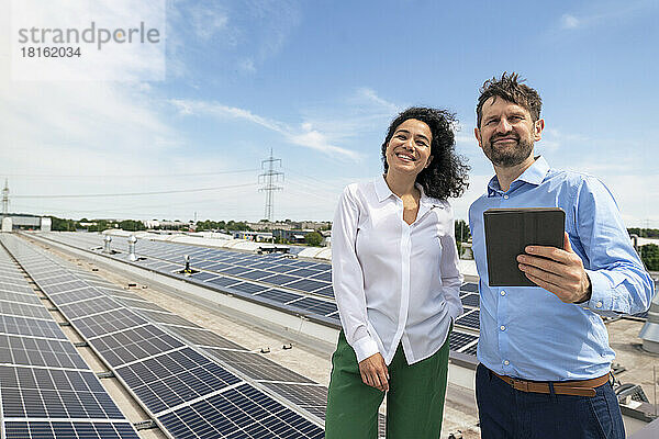 Lächelnder Geschäftsmann mit Tablet-PC und Geschäftsfrau vor Sonnenkollektoren