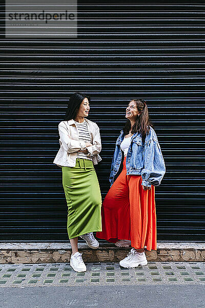 Happy lesbian friends talking to each other in front of shutter
