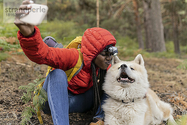 Junge Frau macht Selfie mit Hund  der im Wald sitzt