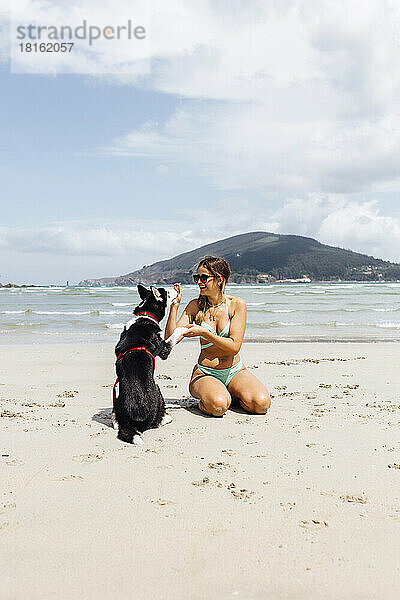 Glückliche junge Frau  die mit Husky am Strand spielt