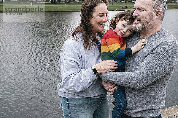 Glückliche Eltern mit ihrer Tochter stehen vor dem See im Park