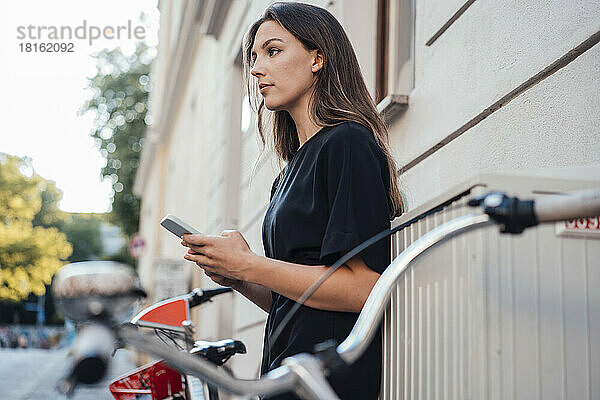 Frau mit Smartphone steht am Fahrrad