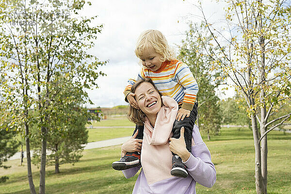 Glückliche Mutter trägt Sohn auf Schultern im Park
