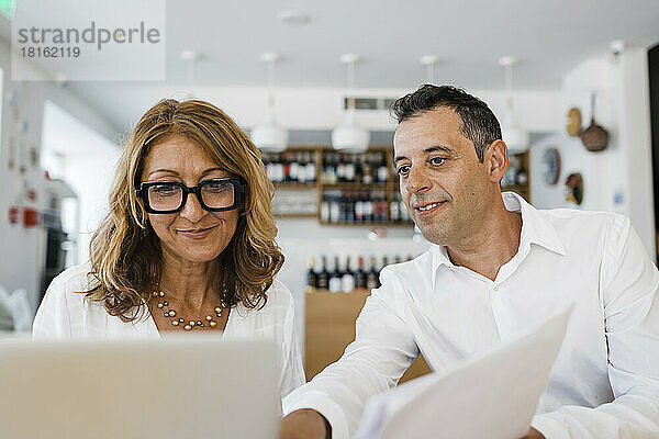 Lächelnder Restaurantbesitzer diskutiert am Laptop mit Kollegen
