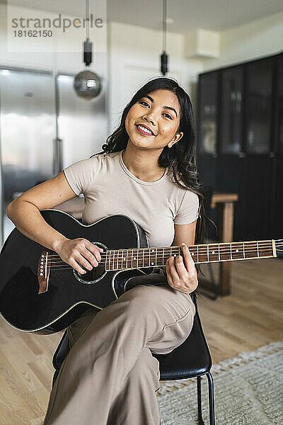 Smiling woman playing guitar at home