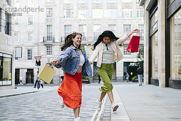 Happy lesbian women with shopping bags running across footpath
