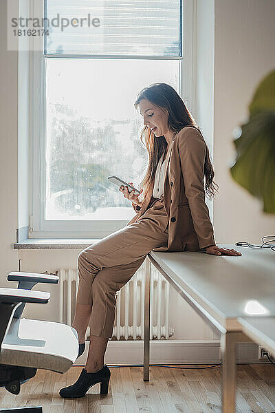 Lächelnder Freiberufler mit Mobiltelefon am Schreibtisch im Heimbüro