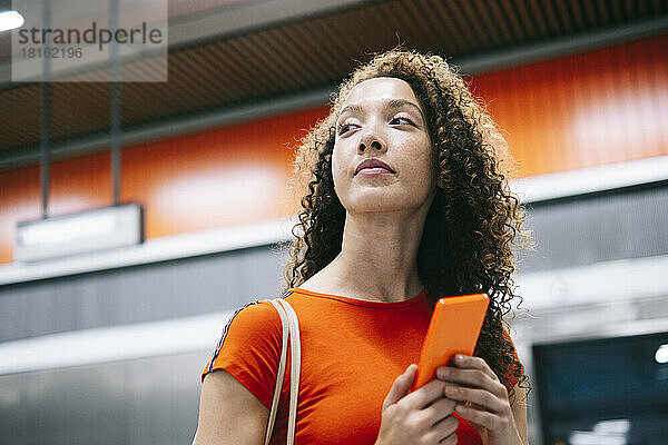 Junge Frau mit Mobiltelefon steht an der U-Bahn-Station
