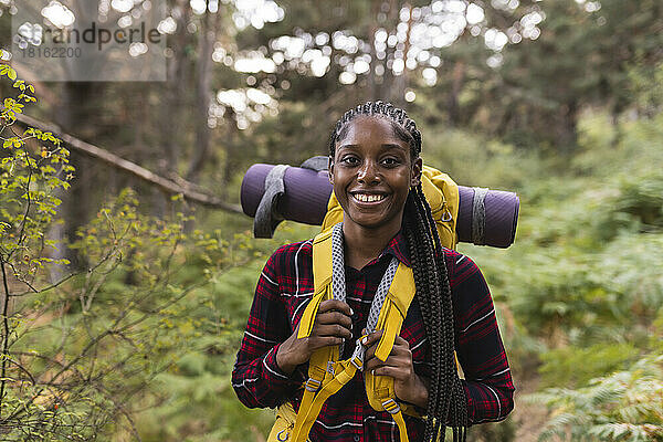 Glückliche junge Frau mit Rucksack steht im Wald
