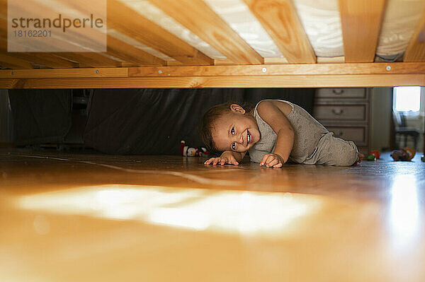 Glücklicher Junge  der zu Hause unter dem Bett schaut