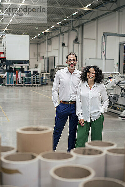 Lächelnde Geschäftsfrau und Geschäftsmann mit den Händen in den Taschen in der Industrie