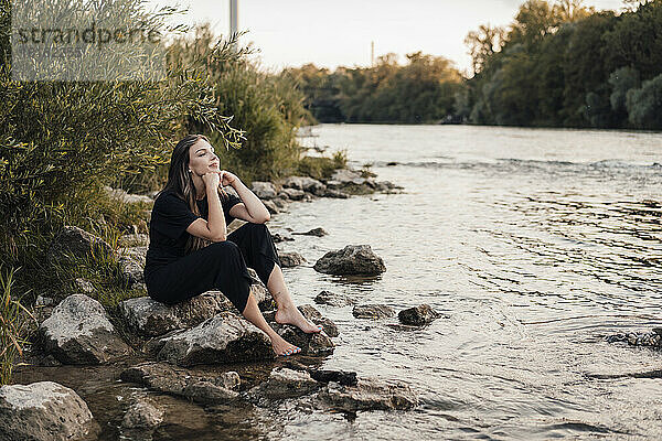 Frau mit den Händen am Kinn sitzt am See