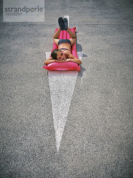 Girl with sunglasses lying on inflatable pool raft over arrow symbol in parking lot
