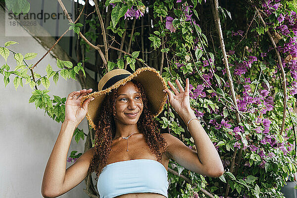 Lächelnde junge Frau mit Hut steht vor der Pflanze