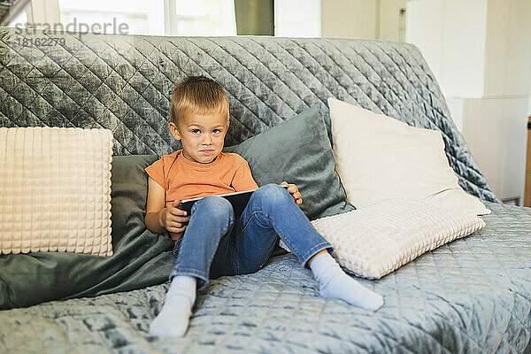 Netter Junge mit Tablet-PC sitzt zu Hause auf dem Sofa