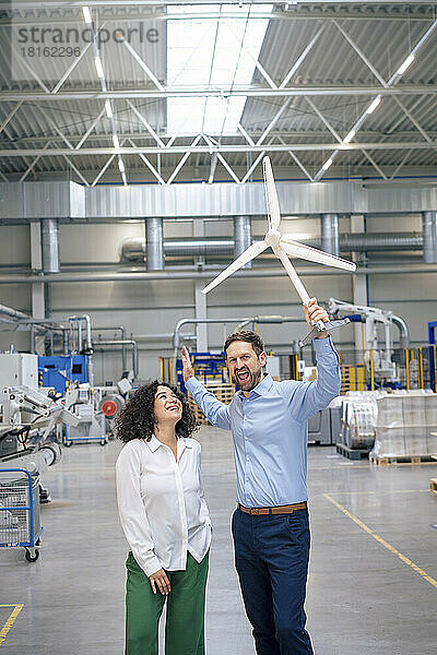 Glücklicher Geschäftsmann hält Windturbinenmodell in der Hand und steht Geschäftsfrau in der Industrie zur Seite