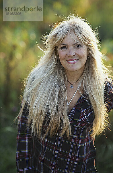 Lächelnde blonde Frau mit langen Haaren an einem sonnigen Tag