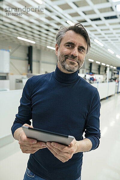 Lächelnder Geschäftsmann mit Tablet-Computer steht in der Industrie