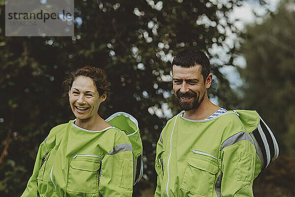 Cheerful beekeeper with colleague wearing green protective suits