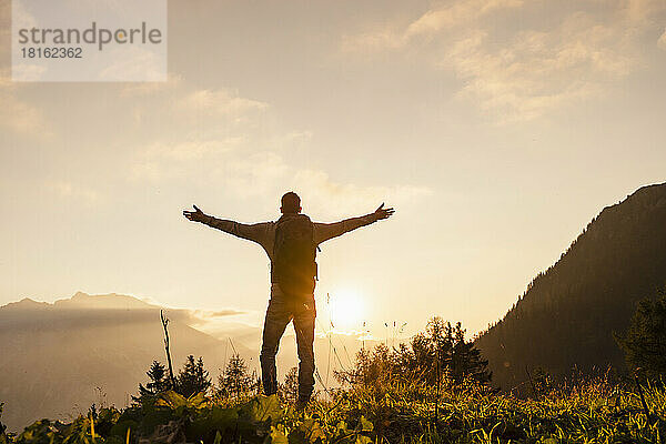Man standing with arms outstretched at sunset