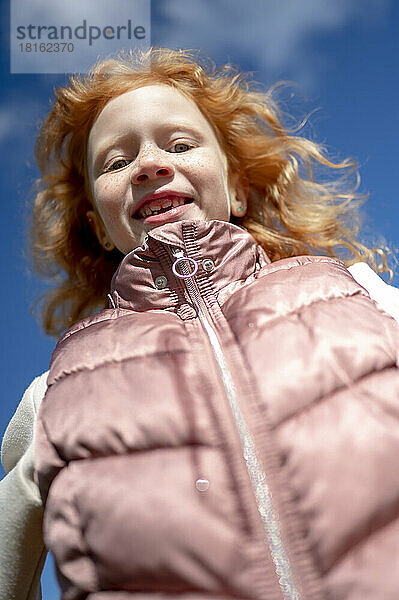 Lächelndes Mädchen in gepolsterter Jacke an einem sonnigen Tag