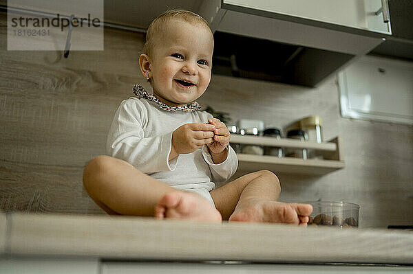 Glückliches süßes Baby  das zu Hause auf der Küchentheke sitzt