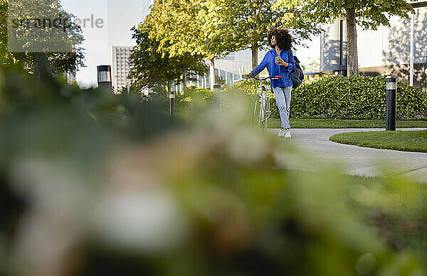 Frau hält Mobiltelefon und steht mit Fahrrad im Park