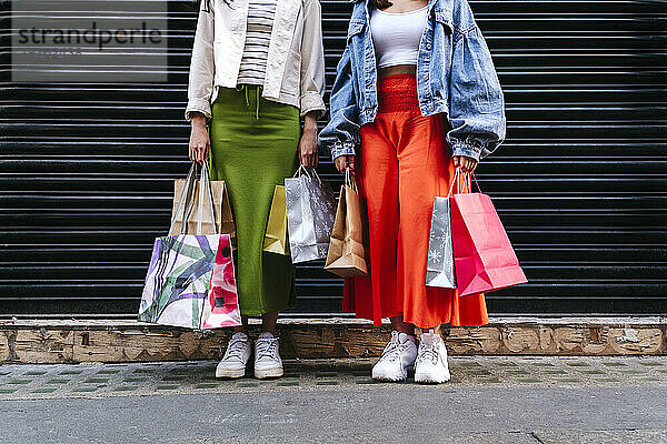 Lesbian couple holding shopping bags in front of shutter