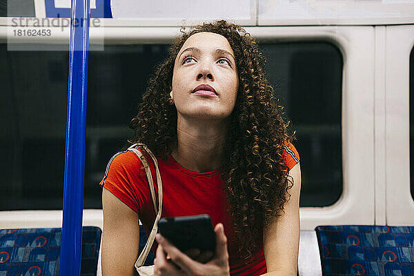 Nachdenkliche junge Frau mit Smartphone sitzt in der U-Bahn