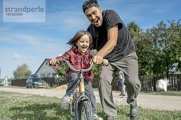Cheerful father teaching happy son to ride bicycle on sunny day