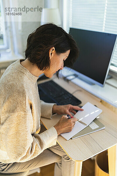 Geschäftsfrau schreibt zu Hause in Notizblock auf dem Tisch