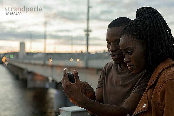 Young couple sharing smart phone at bridge