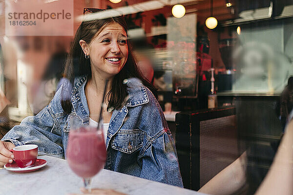Happy woman talking with lesbian friend at cafe seen through window