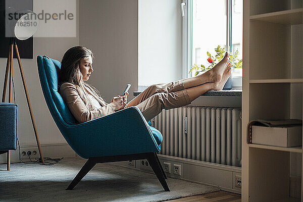 Businesswoman with feet up using smart phone on chair at home