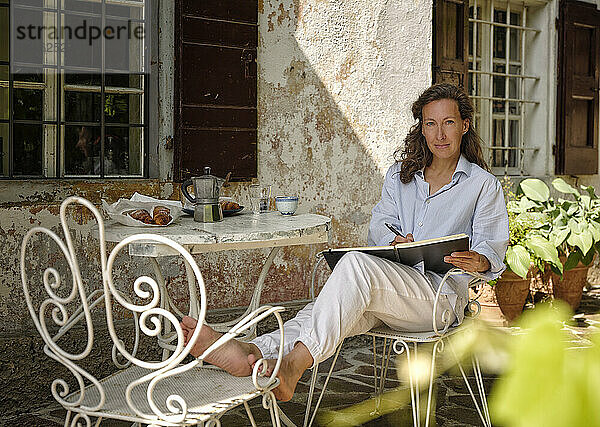 Frau mit Skizzenbuch auf Stuhl auf der Terrasse