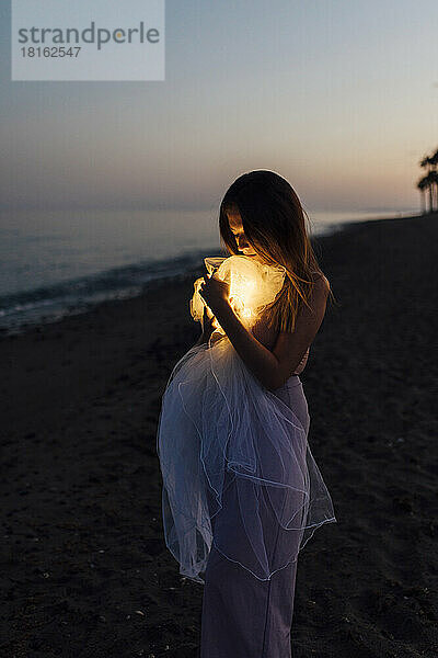 Junge Frau hält Stoffball mit Licht am Strand