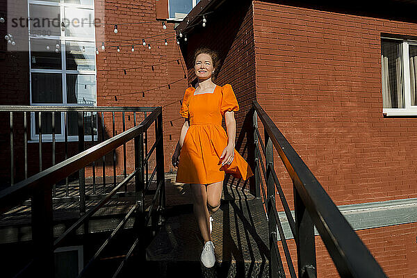 Lächelnde Frau in orangefarbenem Kleid  die die Treppe hinuntersteigt