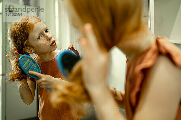 Mädchen bürstet Haare vor Spiegel