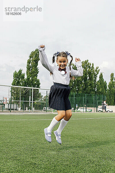Sorgloses Mädchen in Uniform springt auf dem Rasen der Schule