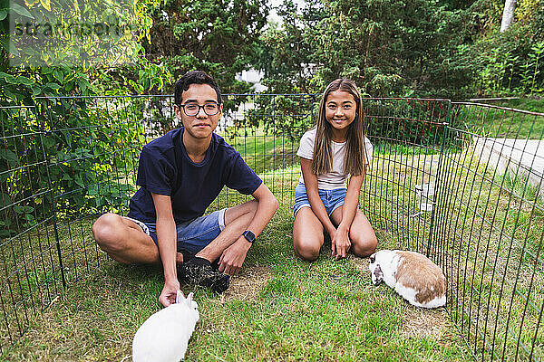 Bruder und Schwester verbringen ihre Freizeit mit Kaninchen inmitten eines Zauns im Hinterhof