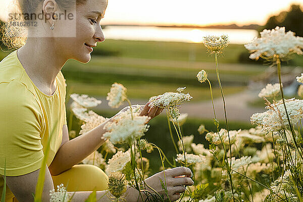 Lächelnde Frau  die weiße Wildblumen betrachtet