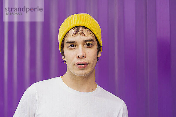 Non-binary person wearing knit hat in front of purple corrugated wall