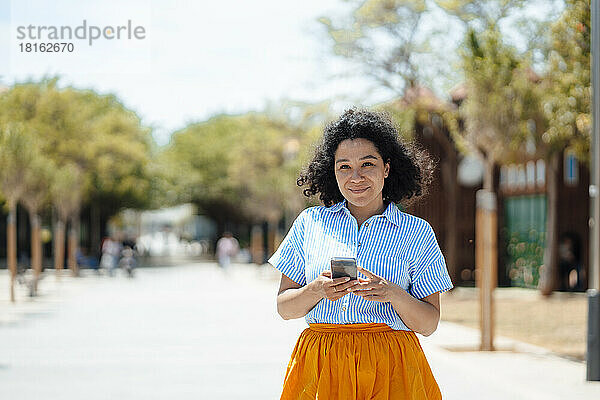 Lächelnde Frau mit Smartphone an einem sonnigen Tag