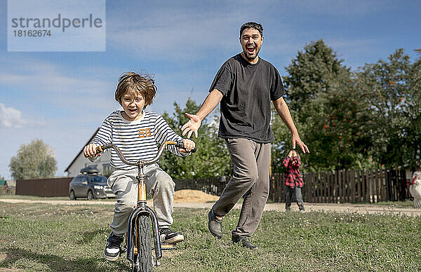 Glücklicher Vater schaut seinem Sohn beim Fahrradfahren an einem sonnigen Tag zu