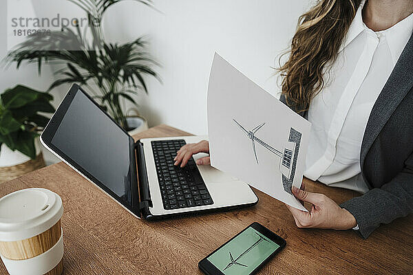 Young businesswoman working in modern office holding plan of windturbine
