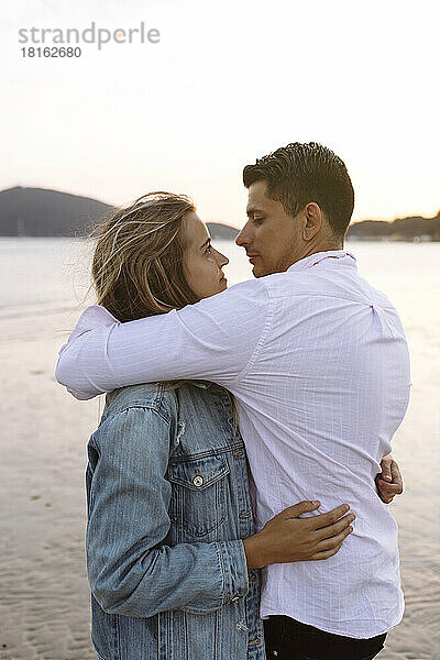 Zärtliches Paar umarmt sich am Strand bei Sonnenuntergang