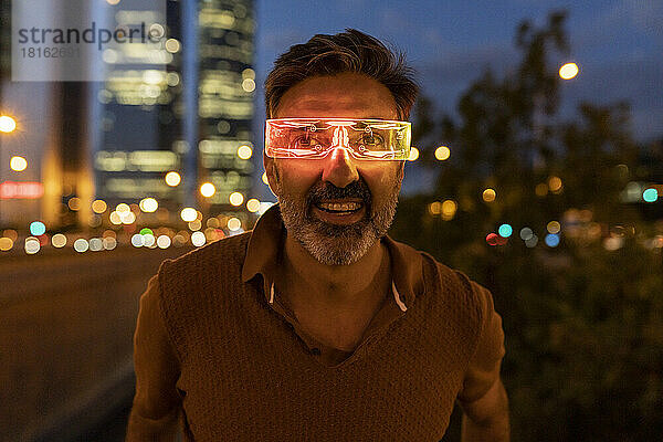 Glücklicher Geschäftsmann  der nachts eine beleuchtete Smart-Brille trägt