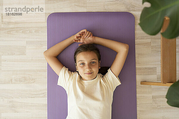 Smiling girl lying on exercise mat at home