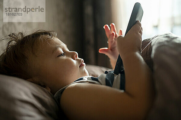 Baby Junge benutzt Handy im Bett liegend