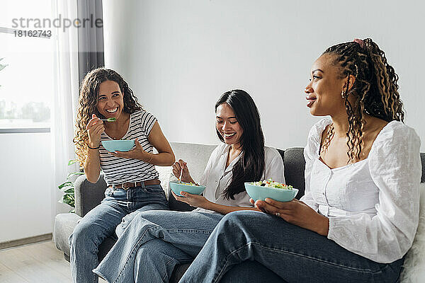 Glückliche Freunde  die zu Hause auf dem Sofa Salat essen